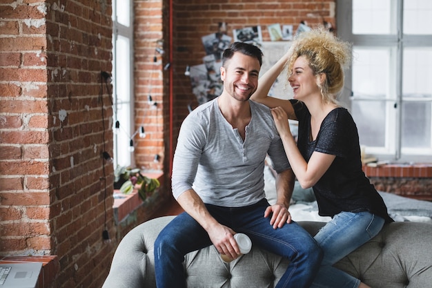 Lindo casal jovem sorrindo e sentado no sofá, enquanto passam algum tempo juntos em casa.