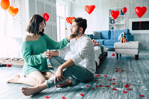 Foto lindo casal lindo e tenro estão se beijando e abraçando enquanto está sentado no chão do quarto com fundo romântico. dia de são valentim. aniversário. encontro. conceito de amor