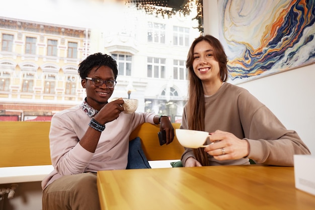 Lindo casal mestiço de adolescentes desfrutando de milk-shake no primeiro encontro da cafeteria