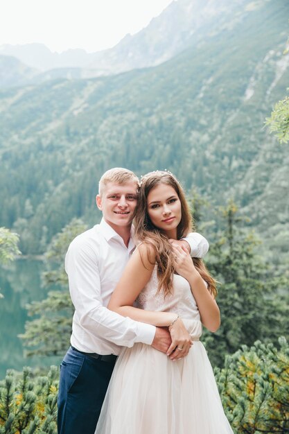 Lindo casal moderno perto de um lago nas montanhas faz fotos de casamento