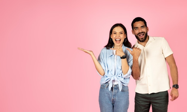 Foto lindo casal multirracial amoroso apontando para espaço livre em rosa