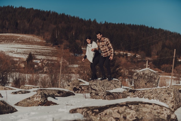 Lindo casal na natureza do inverno andando pelas rochas cobertas de neve contra um céu sem nuvens e árvores nuas Foco seletivo