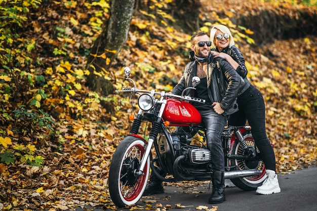 Lindo casal perto de motocicleta vermelha na estrada na floresta