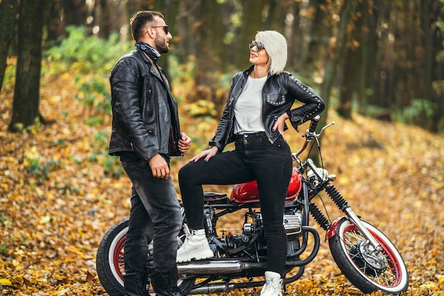 Lindo casal perto de motocicleta vermelha na estrada na floresta