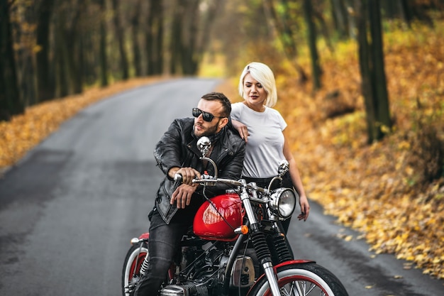 Lindo casal perto de motocicleta vermelha na estrada na floresta