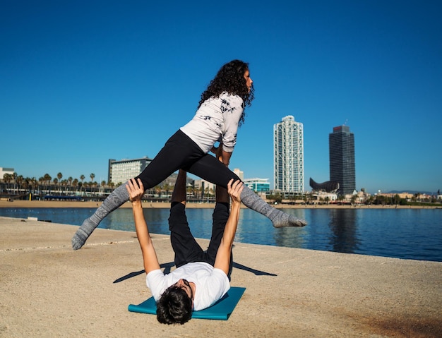 Lindo casal praticando acro ioga pela manhã, ao ar livre, perto do mar. Conceito de equilíbrio e conexão.