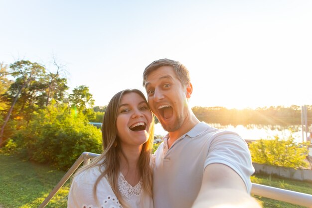 Lindo casal romântico engraçado no fundo da natureza. Mulher jovem e atraente e homem bonito estão fazendo selfie, sorrindo e olhando para a câmera.