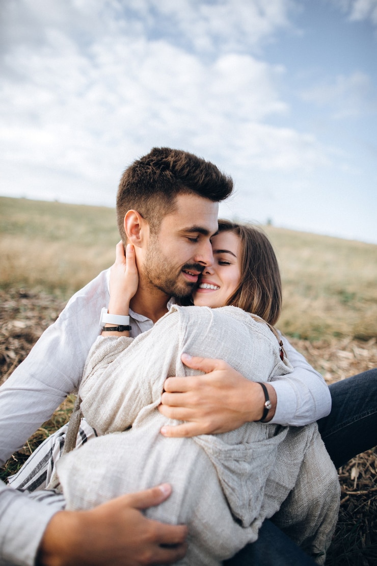 Foto lindo casal se abraçando, beijando e sorrindo contra o céu sentado na grama. espaço para texto