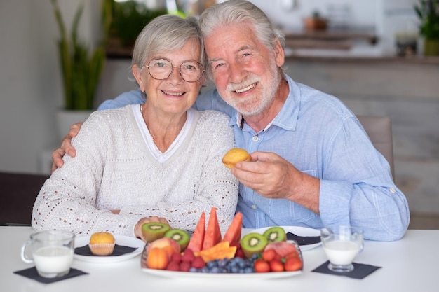 Foto lindo casal sênior aposentado caucasiano tomando café da manhã em casa com leite de frutas frescas da estação e conceito de alimentação saudável de cupcake