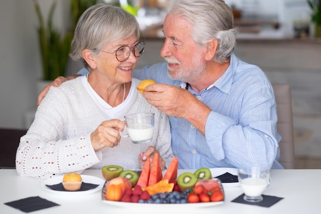 Lindo casal sênior aposentado caucasiano tomando café da manhã em casa com leite de frutas frescas da estação e conceito de alimentação saudável de cupcake