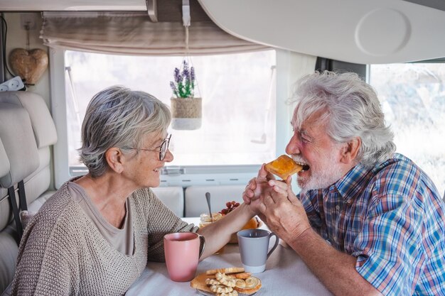 Lindo casal sênior feliz em férias de viagem sentado dentro de um campista desfrutando de café da manhã juntos