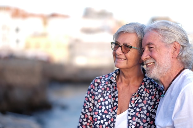 Lindo casal sênior sorrindo ao ar livre no mar ao pôr do sol llight, olhando para a câmera. casal caucasiano de cabelos brancos