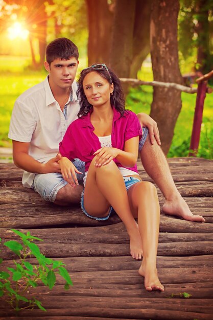 Lindo casal sentado na velha ponte de madeira e olhando para o estilo do instagram da câmera