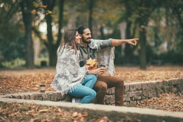 Lindo casal sorridente desfrutando no parque da cidade ensolarada em cores de outono, olhando um ao outro. Eles estão se divertindo com folhas amarelas.