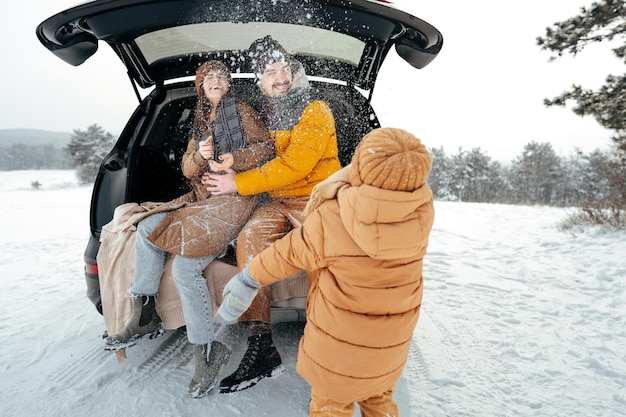 Lindo casal sorridente sentado no porta-malas do carro na floresta de inverno