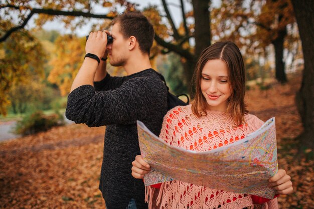 Lindo casal viajando juntos. ela segura o mapa e o estuda. ele olha nos binóculos em uma direção. pose de mulher.