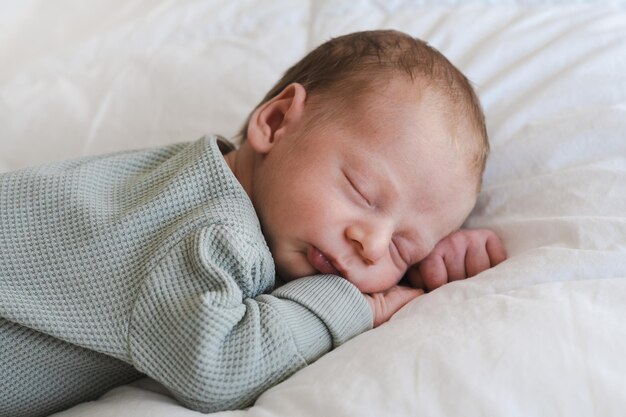 Lindo caucásico varios días de edad recién nacido durmiendo boca abajo sobre una sábana blanca en casaadorablecalm inn
