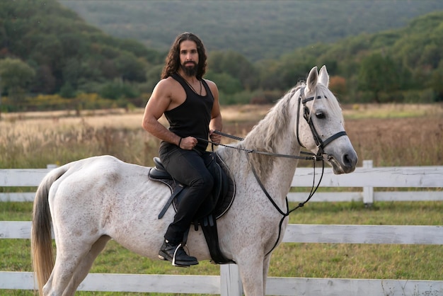 Lindo cavalo com cavaleiro homem trotando no campo outonal. Conceito de amor equestre e animal. Cavaleiro no cavalo árabe cinza no campo. Homem barbudo bonito cavalgando na fazenda.