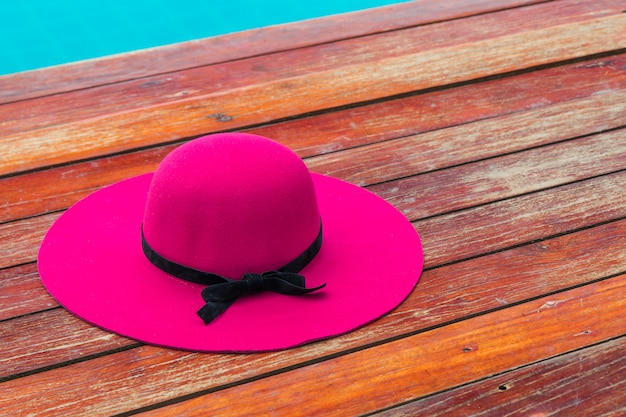 Lindo chapéu-de-rosa com laço preto em um piso de madeira à beira da piscina