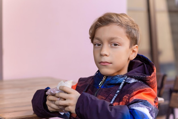 Lindo chico adolescente de moda comiendo kebab en un café de la calle