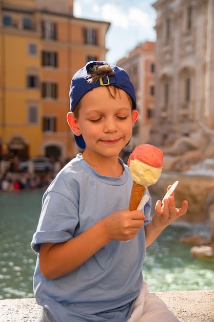 Lindo chico alegre de 7 años comiendo helado helado cerca de la Fontana de Trevi en Roma Italia