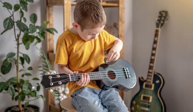 Lindo chico alegre está tocando el ukelele en la sala de música Alegre aprendiendo a tocar instrumentos musicales guitarra hawaiana