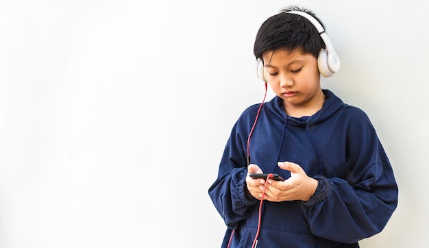 Lindo chico asiático en una sudadera con capucha posando escuchando música y auriculares sobre fondo blanco.