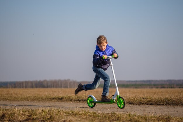 Foto lindo chico europeo montando y haciendo trucos en scooter mientras camina