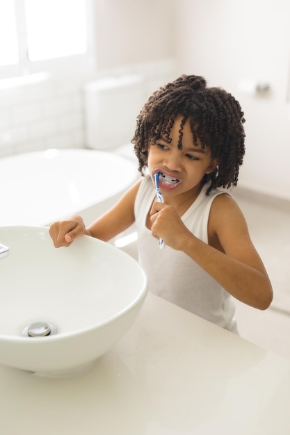 Lindo chico hispano con pelo negro rizado cepillándose los dientes en el baño de casa