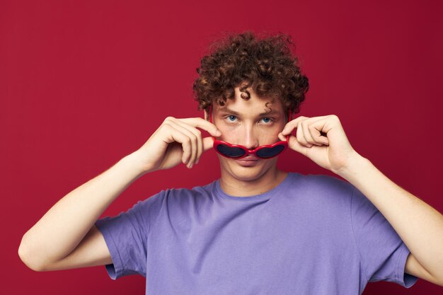 Lindo chico pelirrojo gestos con las manos gafas en forma de corazón posando fondo rojo