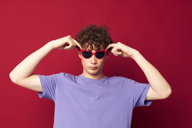 Lindo chico pelirrojo gestos con las manos gafas en forma de corazón posando fondo rojo