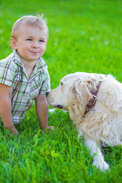 Lindo chico rubio de dos años con golden retriever en la hierba