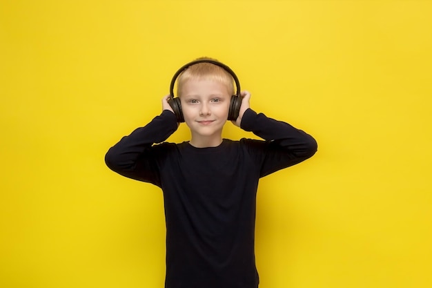 Lindo chico rubio escuchando música o podcast en auriculares con fondo amarillo