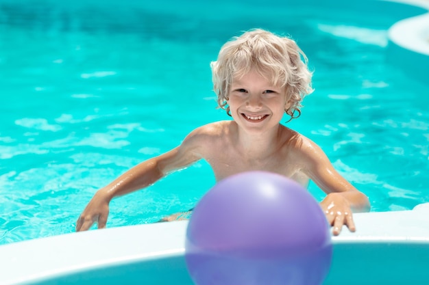 Lindo chico rubio rizado sonriendo mientras nada en la piscina