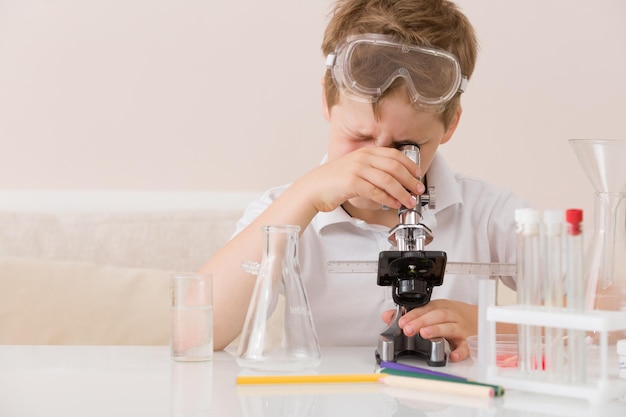 Lindo colegial de primaria mirando al microscopio en su escritorio en casa. Ciencias. concepto de educación