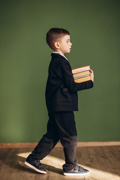 Lindo colegial vistiendo uniforme escolar y sosteniendo libros