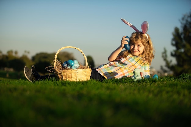 Lindo conejito niño niño con orejas de conejo Niño con huevos de pascua y canasta en la hierba Niño niño cazando huevos de pascua tendido en la hierba