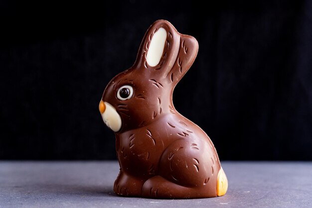 Foto lindo conejo de pascua de chocolate en fondo oscuro negro con luz natural suave