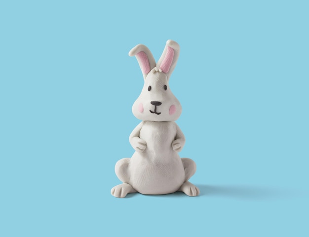 Lindo conejo sentado hecho de plastilina blanca sobre un fondo azul Conejo de pascua hecho a mano en arcilla