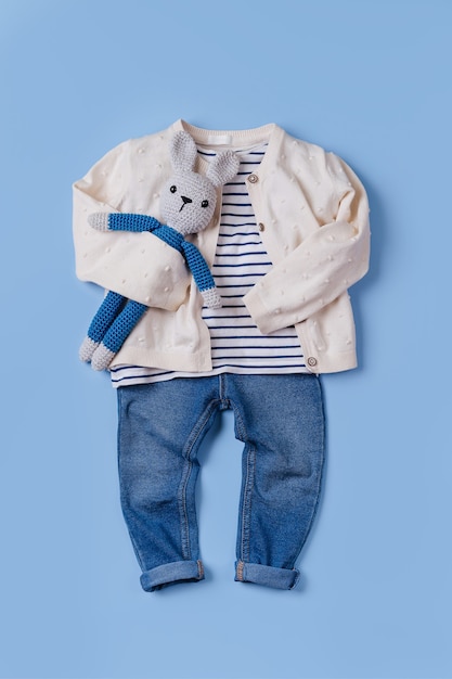 Foto lindo conjunto de roupa de outono para crianças. jaqueta e calça jeans com coelhinho de brinquedo sobre fundo azul.