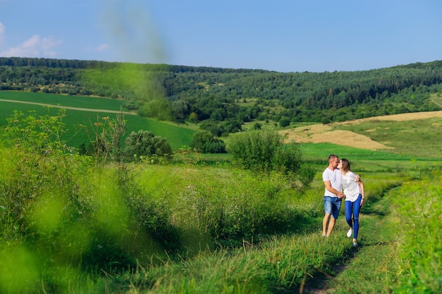 Lindo dia de sol. prado com grama verde e floresta. casal apaixonado, caminhando e beijando.