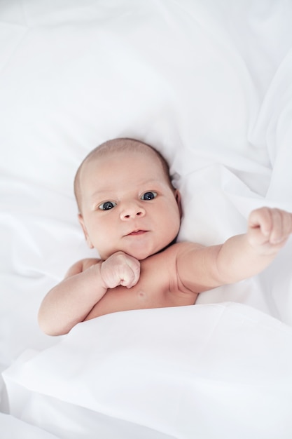 Foto lindo y divertido bebé recién nacido despierto en la cama