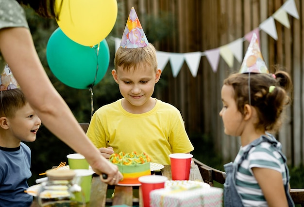 Lindo y divertido niño de nueve años celebrando su cumpleaños con familiares o amigos y comiendo pastel casero en una fiesta de cumpleaños para niños en el patio trasero