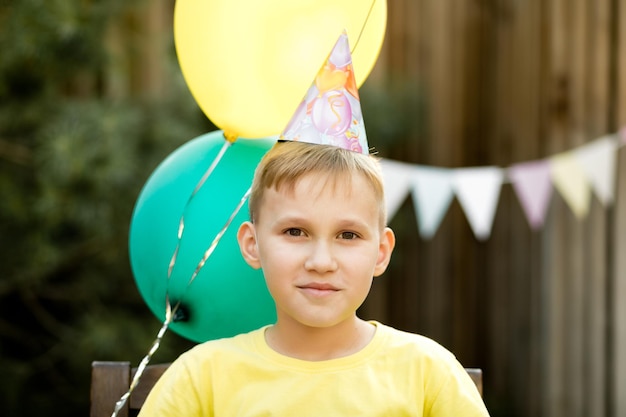 Lindo y divertido niño de nueve años celebrando su cumpleaños con familiares o amigos en una fiesta de cumpleaños en el patio trasero Niño con sombrero de fiesta y sosteniendo un globo en una mano