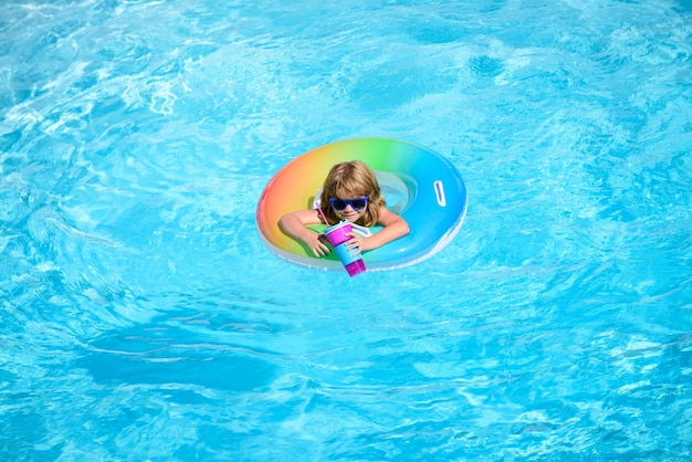 Lindo y divertido niño pequeño con un colorido traje de baño y gafas de sol relajándose con un flotador de anillo de juguete
