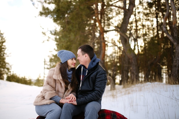 Lindo e feliz casal apaixonado, sentado em um cobertor no inverno em um bosque nevado