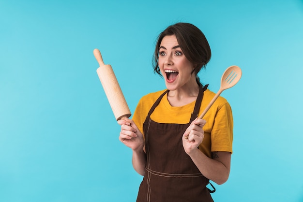 lindo, emocionado, sorprendido, mujer joven, chef, tenencia, rodillo, y, cuchara de madera, aislado, encima, pared azul.