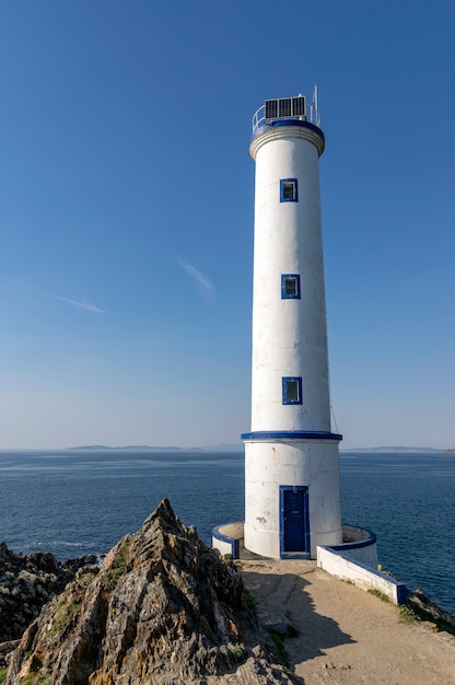 Lindo farol branco e azul nas rochas com o mar ao fundo em um dia ensolarado