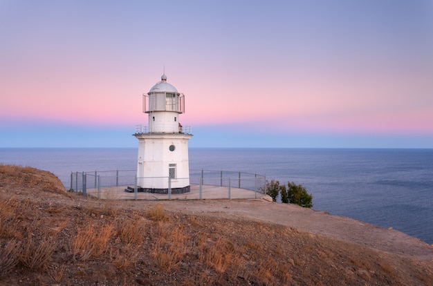 Lindo farol branco na costa do oceano ao pôr do sol