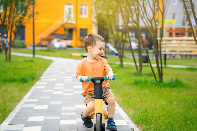 Un lindo y feliz niño pequeño de dos o tres años monta una bicicleta o una bicicleta de equilibrio en un complejo residencial en un soleado día de verano Un niño activo jugando afuera